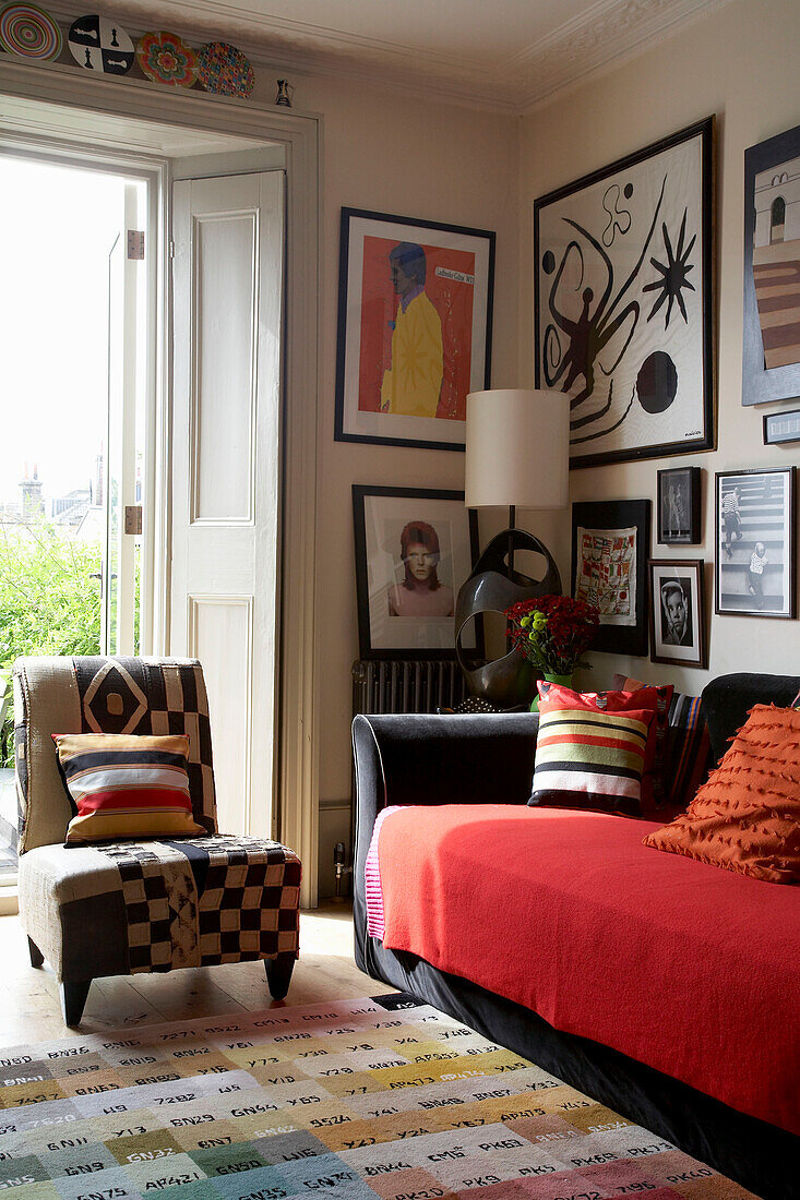 Collection of artwork displayed above black sofa with red throw