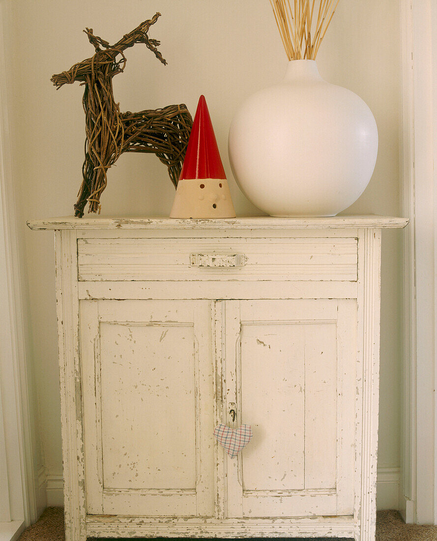 A detail of a country bedroom a distressed painted cabinet ceramic vase twig Reindeer figure
