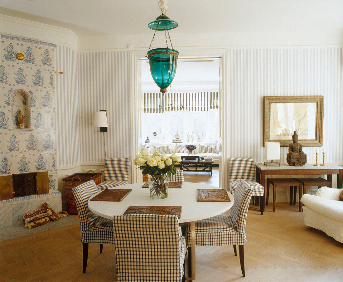 Runder Tisch mit karierten Stühlen in einem Esszimmer mit traditionellem schwedischen Kachelofen