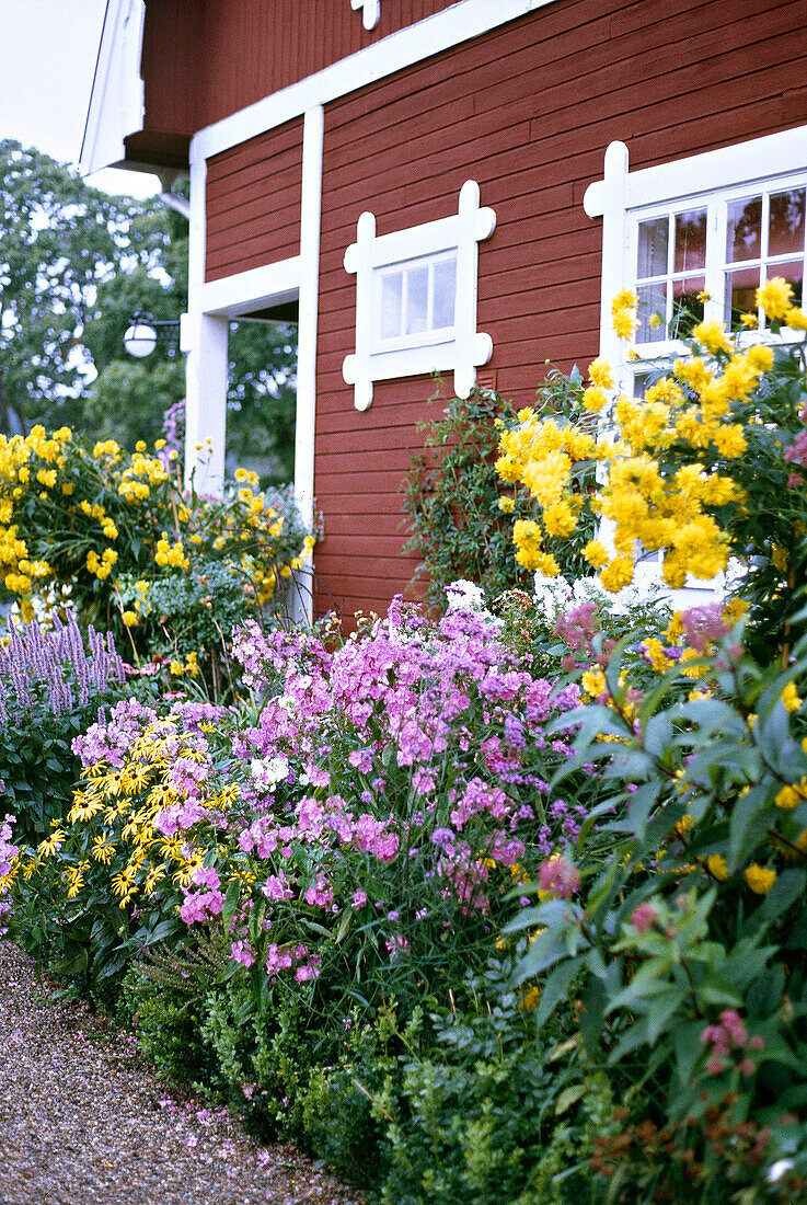 Blühendes Blumenbeet neben rot gestrichenem Holzhaus