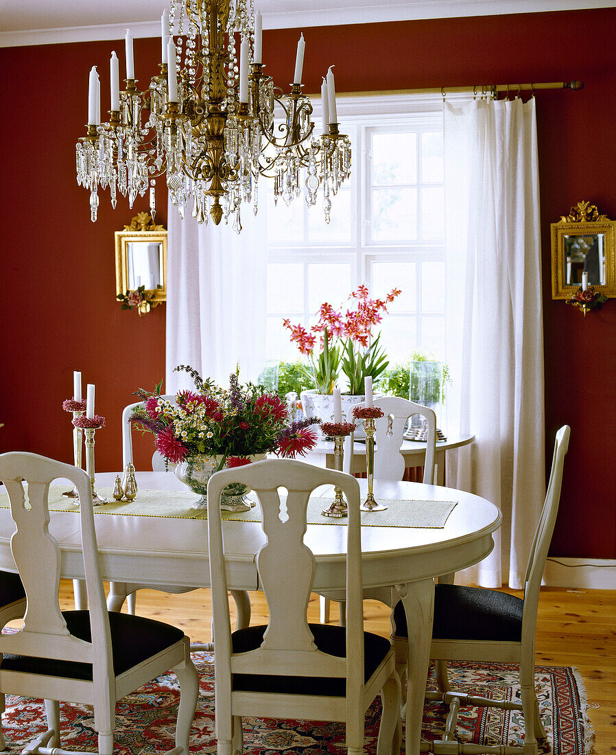 Traditionelles rotes Esszimmer mit weiß gestrichenem Tisch, Stühlen und Glaskronleuchter