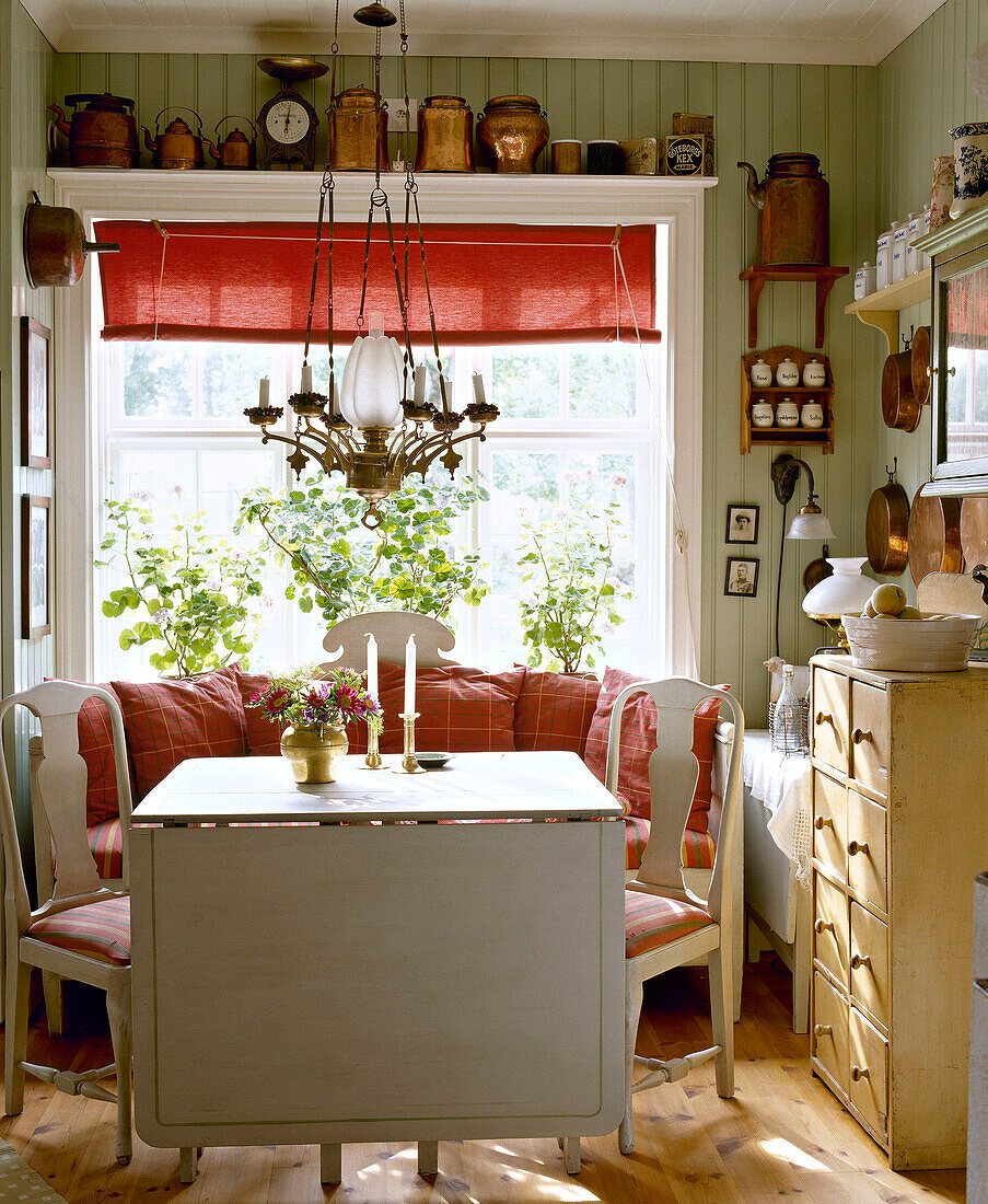 Frühstücksraum im Landhausstil mit grün getäfelten Wändenn Tisch, Stühlen, Fensterbank und roter Jalousie