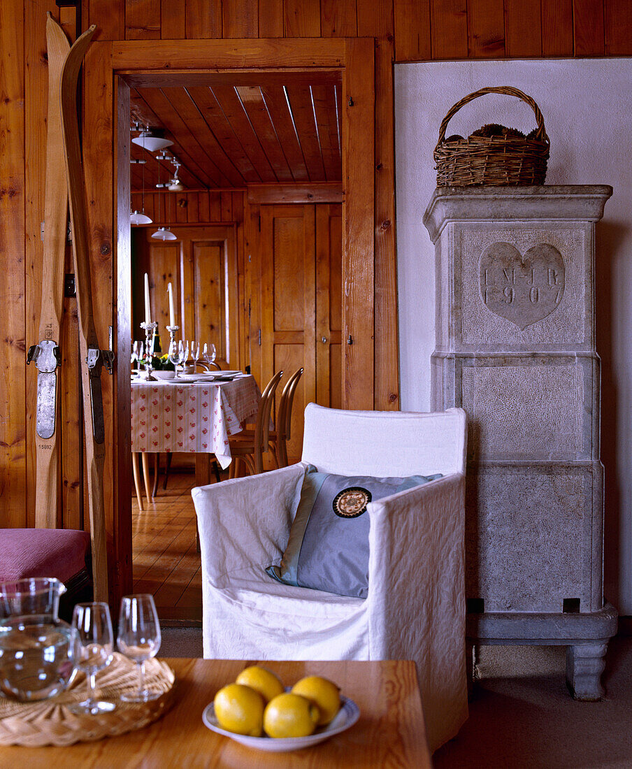 Wohnzimmer in schweizer Chalet mit Holzvertäfelung, Sessel und Blick durch eine geöffnete Tür auf gedeckten Esstisch