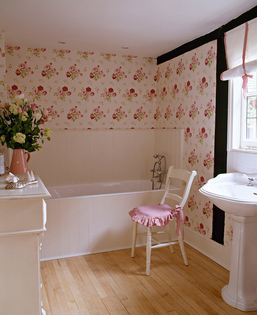 Bathtub and washbasin in pink bathroom with floral wallpaper