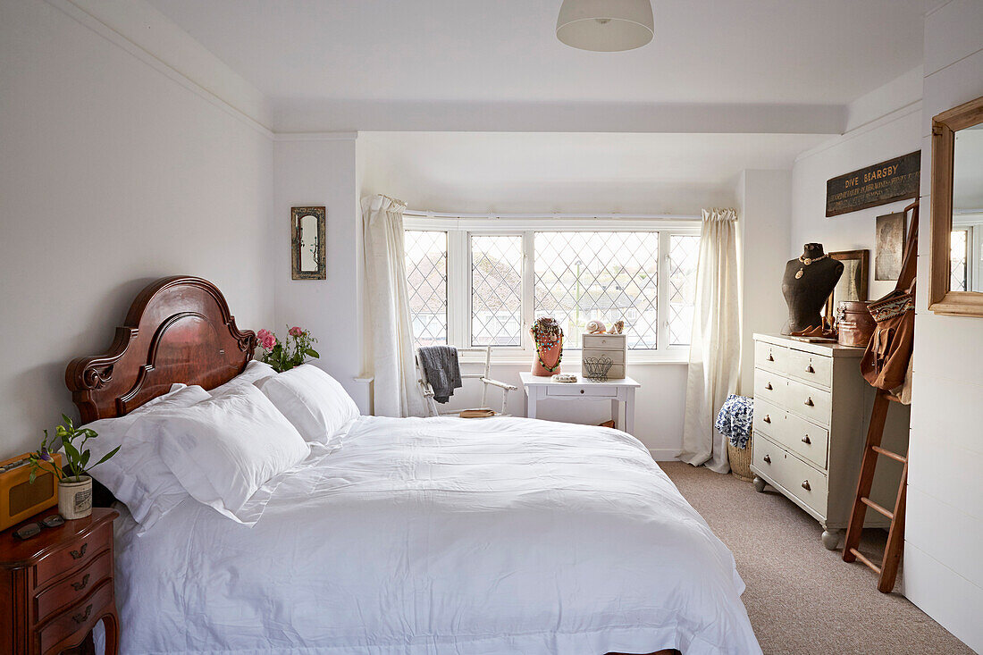 Weißes Doppelbett mit Holzkopfteil in einem Schlafzimmer mit Bleiglasfenster in Shoreham by Sea, West Sussex, UK