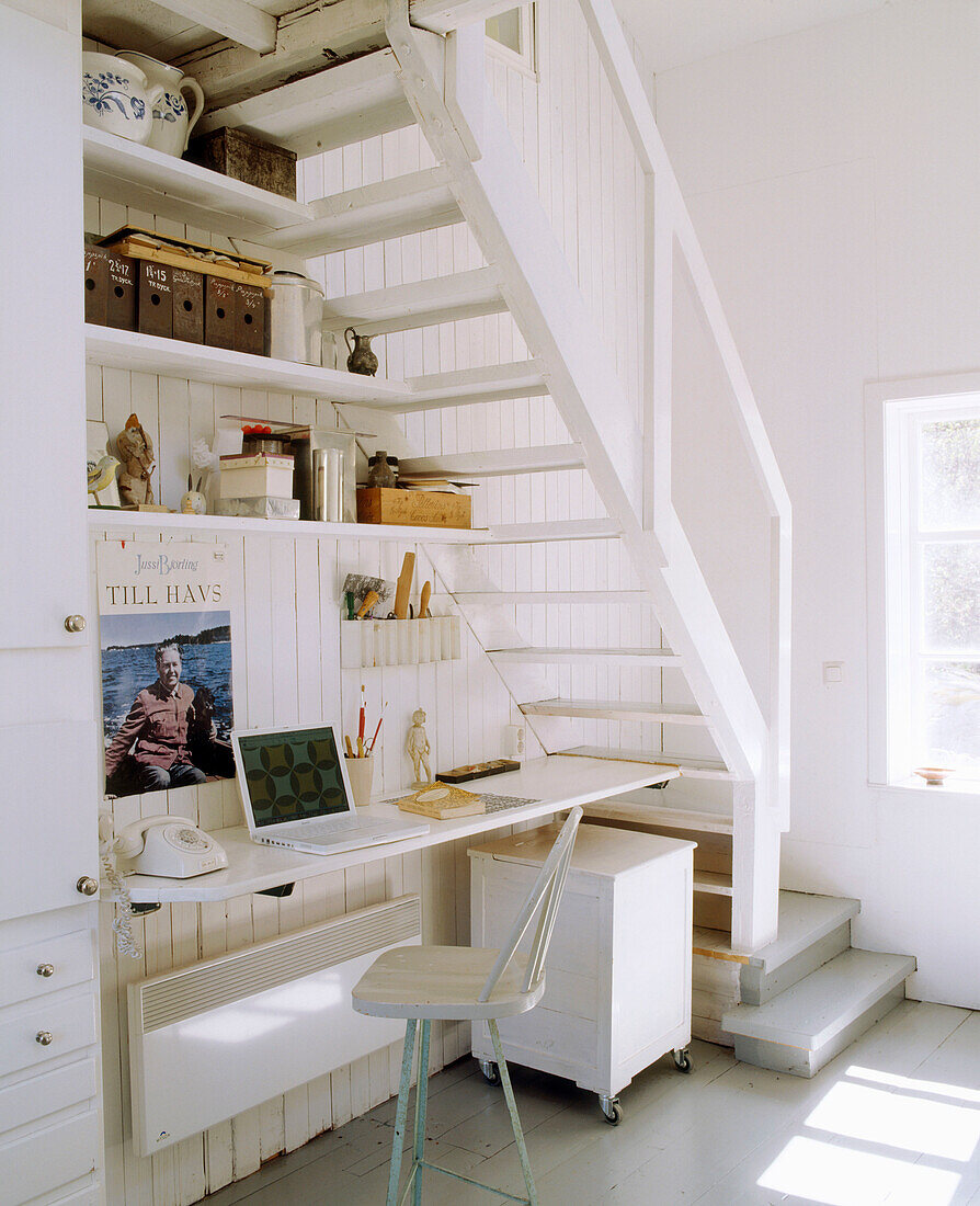 Home office space with a desk and bookshelves underneath the white painted stairway