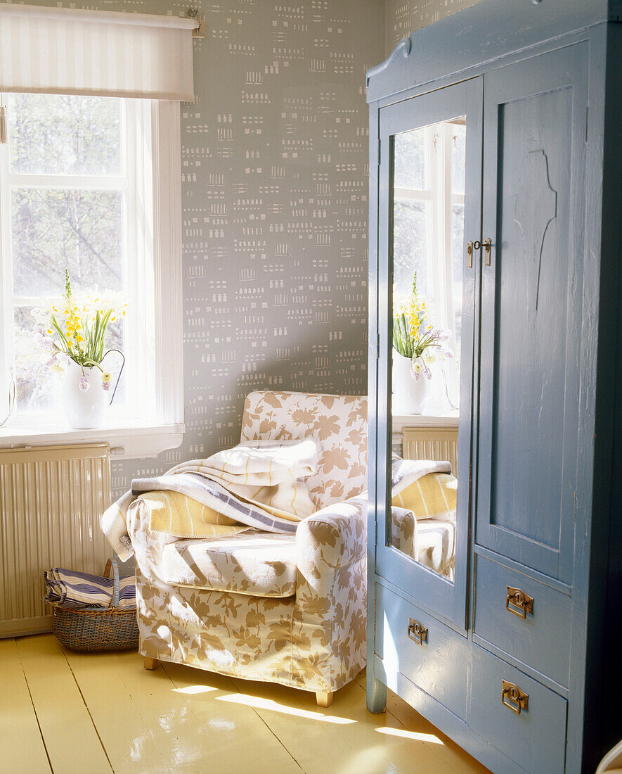Blauer Kleiderschrank und Sessel im Sonnenlicht in einem Wohnzimmer im Landhausstil