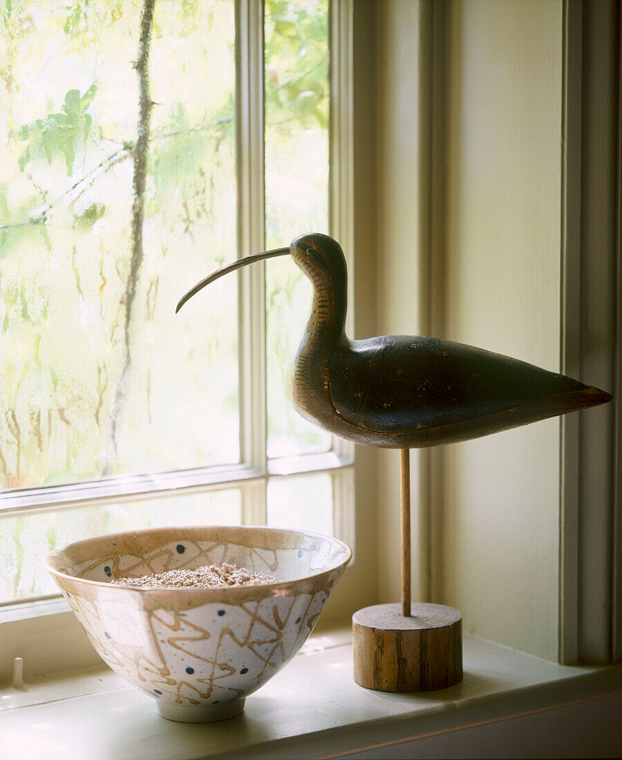 Detail eines Fensters im Landhausstil mit einer Keramikschale und einem hölzernen Vogelköder auf der Fensterbank
