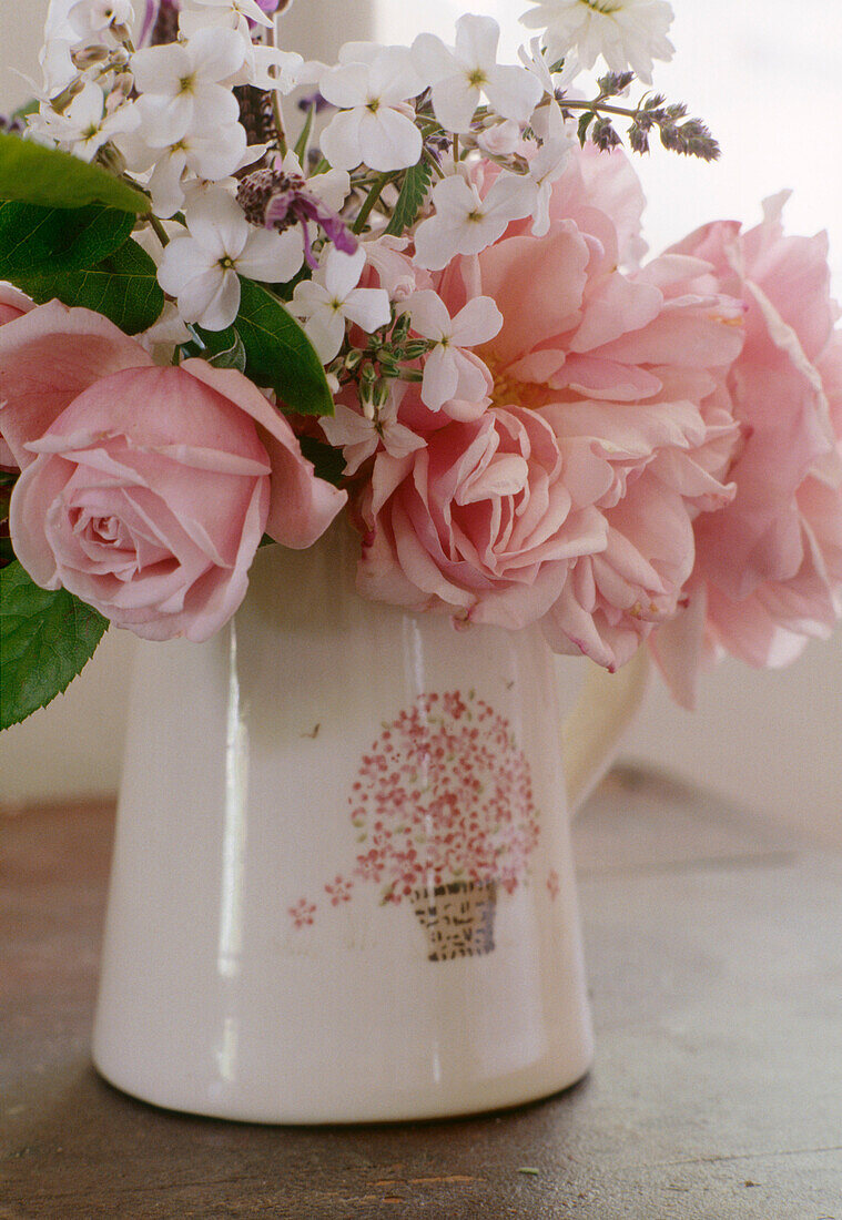 A detail of a flower arrangement of pink roses and white flowers placed in a ceramic jug