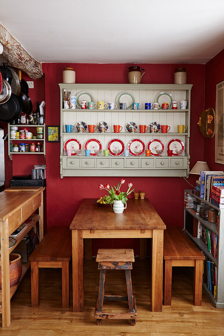 Wandschrank mit Holzsitzbänken und Tisch in der roten Küche eines Hauses in Bridport, Dorset, Großbritannien