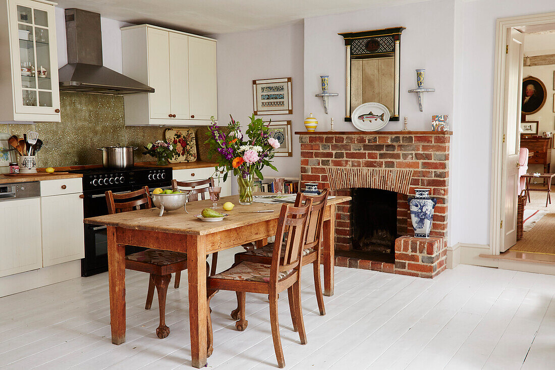 Wooden table and chairs with exposed brick fireplace in kitchen of 17th century Hampshire home, UK