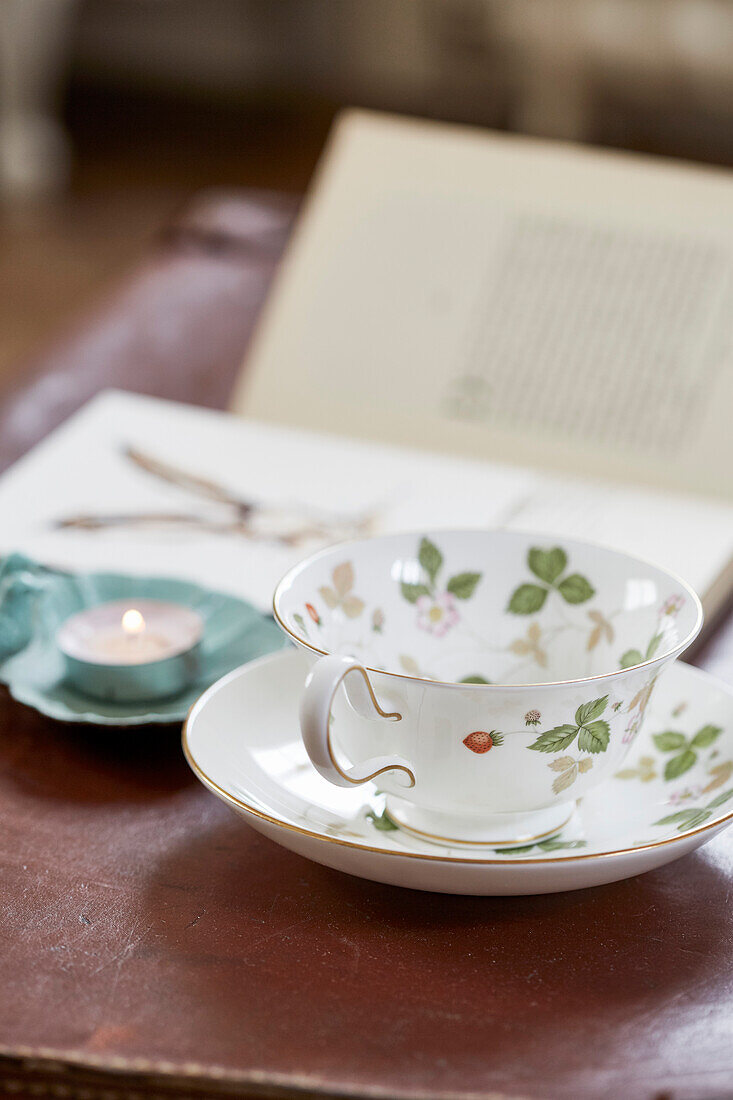 Tasse mit Untertasse, Teelicht und Buch in einem Bauernhaus in Kent, UK