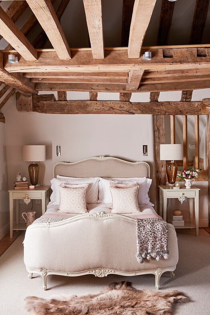 Antikes französisches Bett mit Lampen und Fellteppich in einem unter Denkmalschutz stehenden Bauernhaus mit Holzbalken (Grade II) in Kent, UK