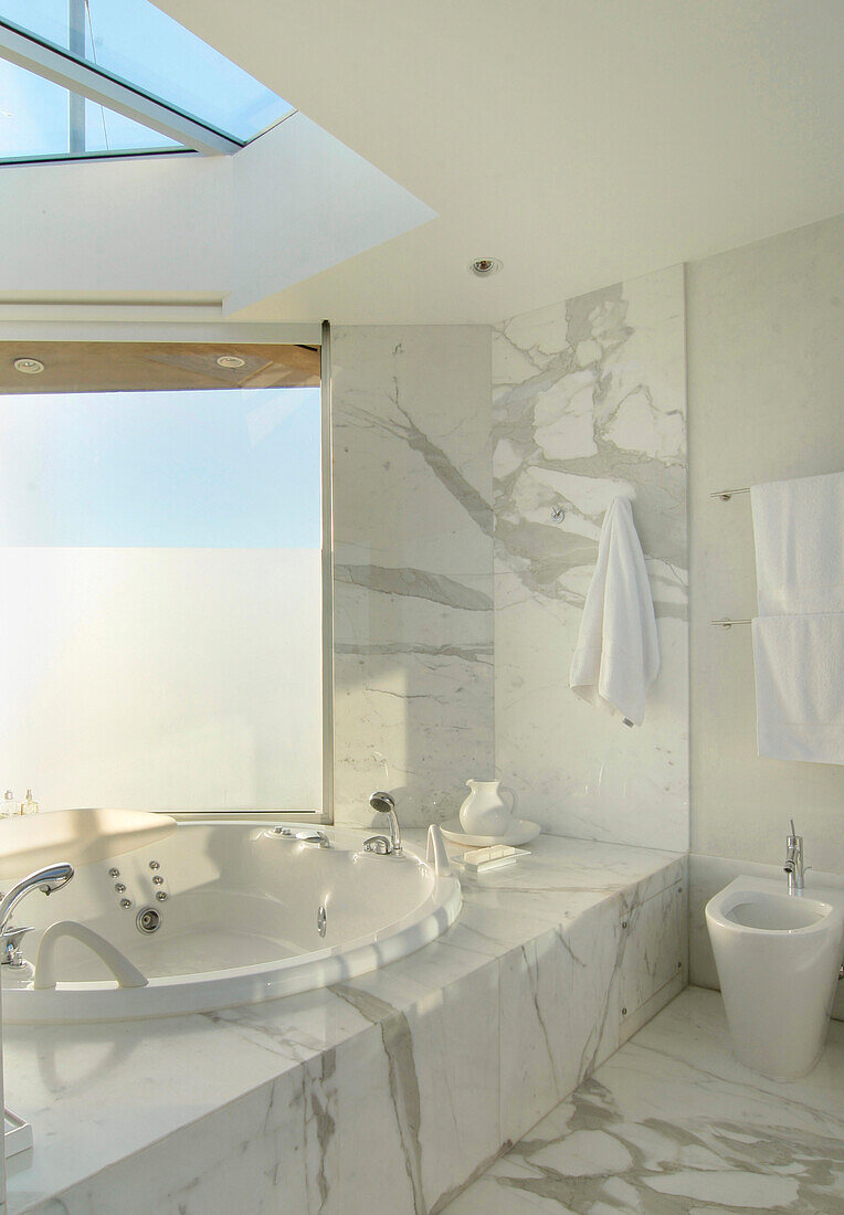 Bathroom with golden Calacata marble Jacuzzi bath surround with shower and skylight above