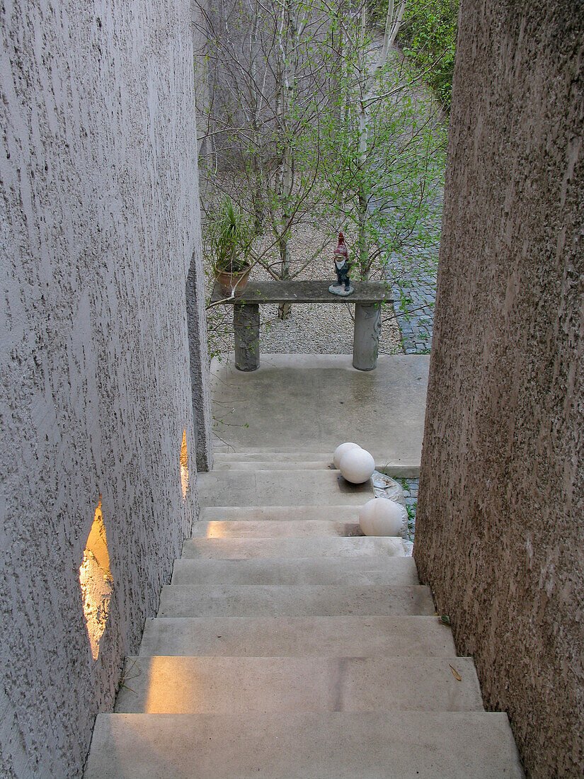 Blick über eine Treppe hinunter zum Garten im Zen-Stil mit strukturierten Betonwänden und Kies