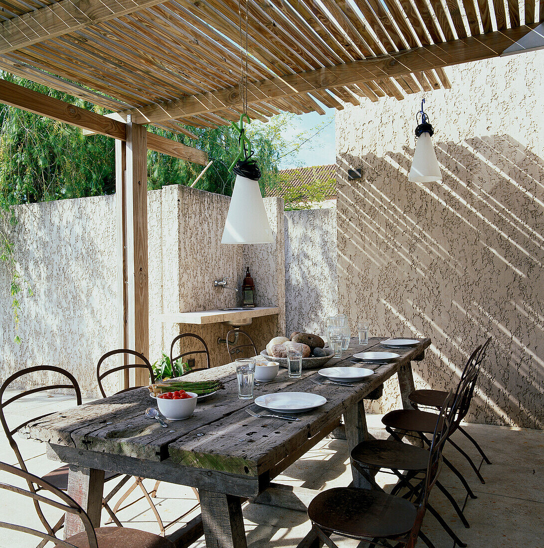 Outdoor dining area with slatted wood arbour and vintage table and chairs and a sink