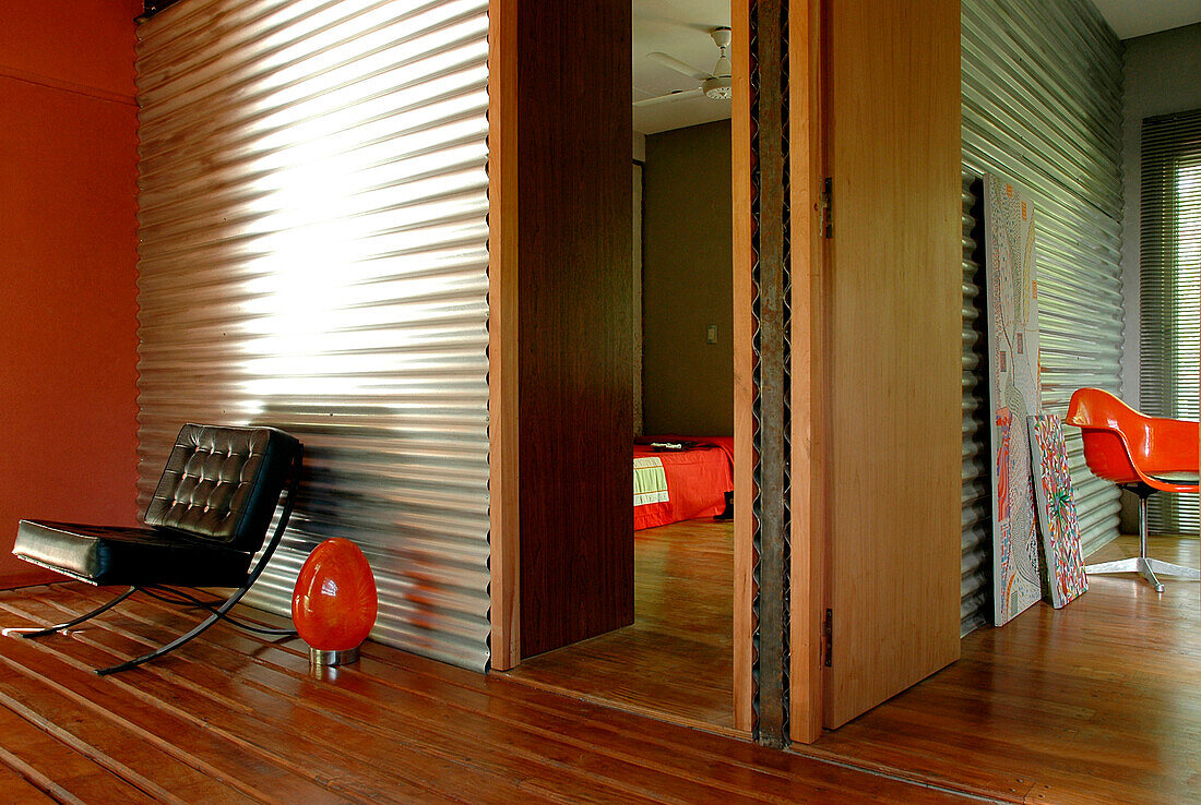 Metal sheeting on walls of entrance hall contrast with a wooden floor laid as a deck with gaps between the boards