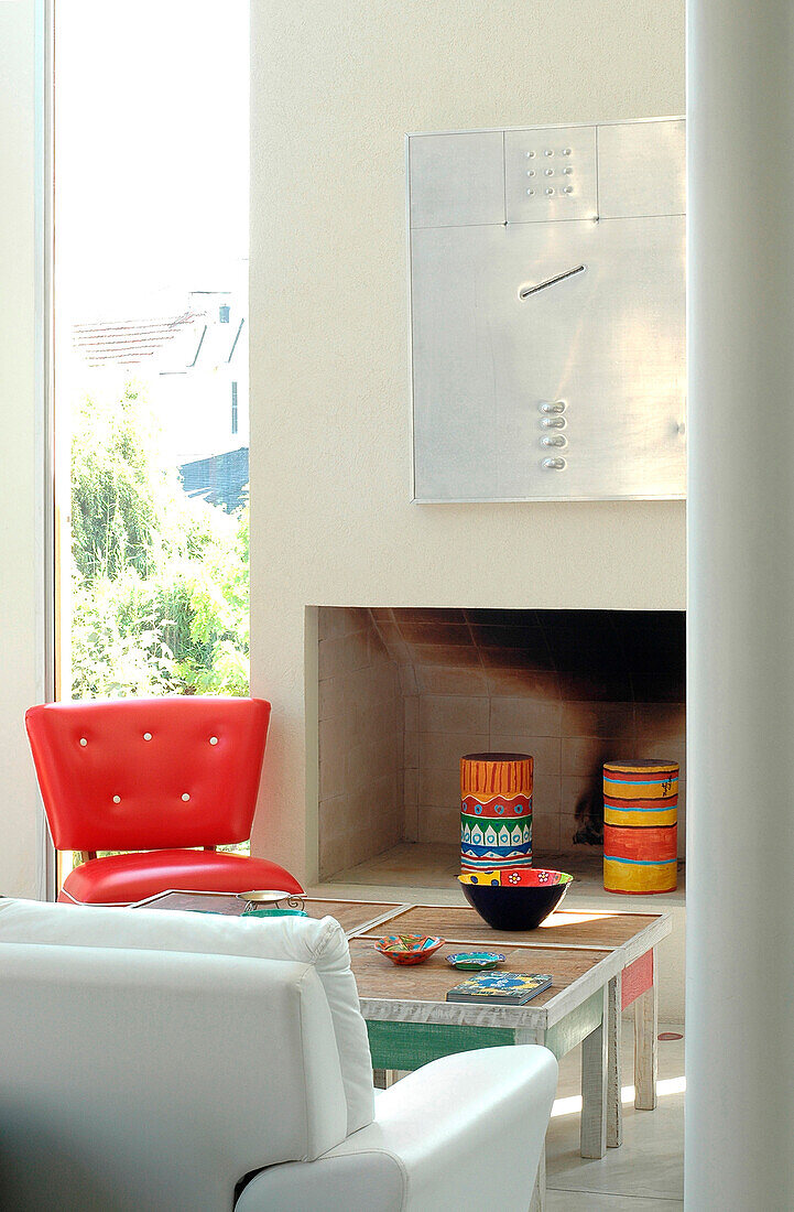 1960s red chair with painted wood coffee table at concrete fireplace with aluminium art piece and double height windows