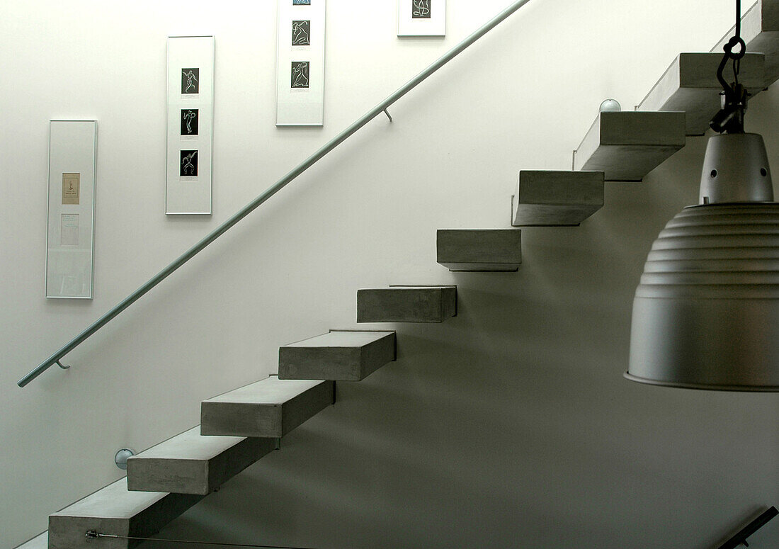 Schwebende Treppe mit Betonstufen und Handlauf aus Zement mit Kunstwerken und Metallpendellampe