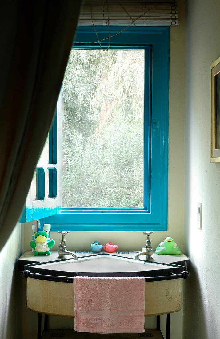 Antiker Waschtisch unter offenem Fenster mit türkisfarbenem Rahmen