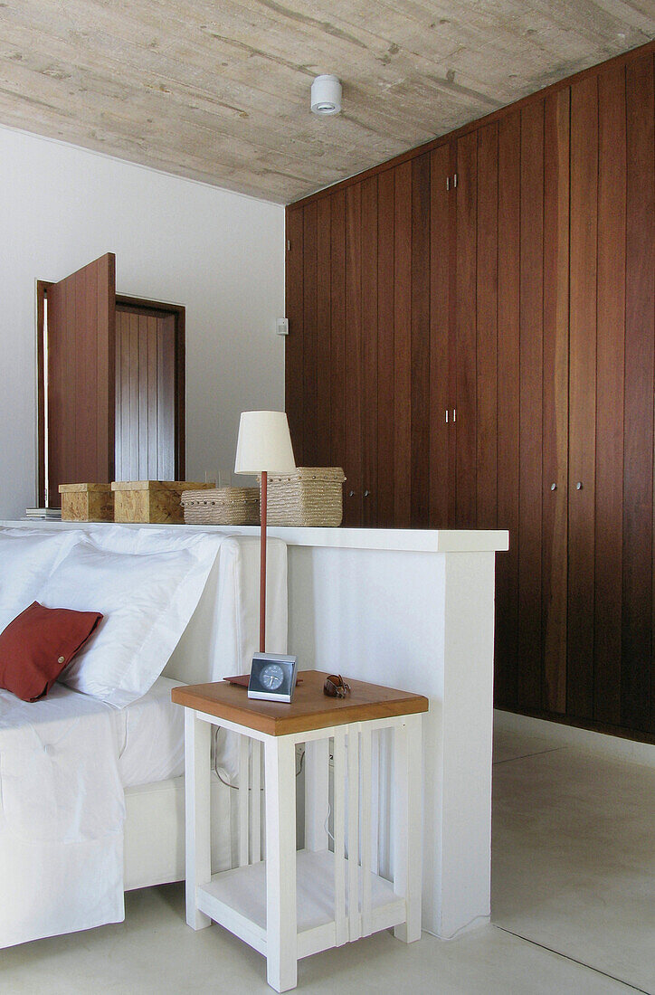 Weiß gestrichenes Bett mit freistehendem Kopfteil in Schlafzimmer mit Einbauschränken aus Holz
