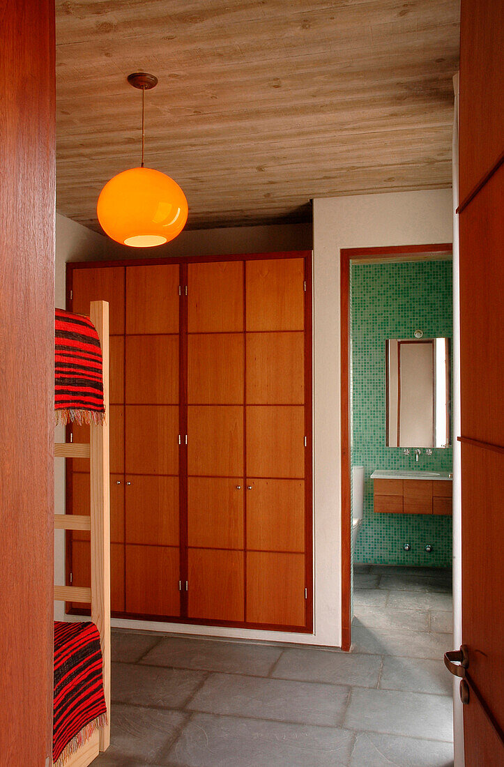 Etagenbetten und Kleiderschränke in einem Gästezimmer mit orangefarbener Deckenleuchte und grün gefliestem Bad