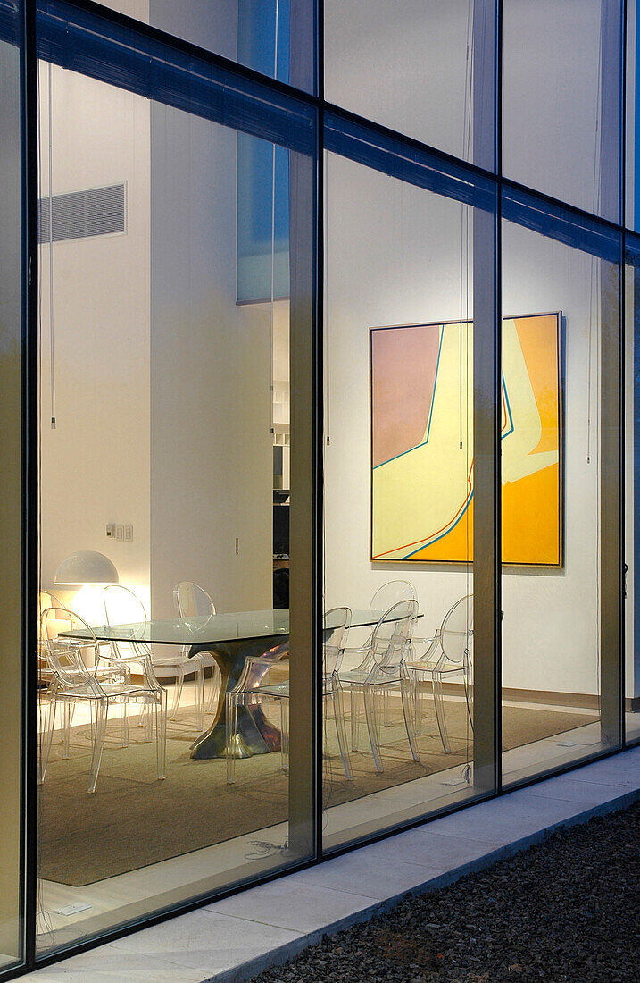 Blick durch die Glaskubusfassade auf Tisch und Stühle im Esszimmer mit einem Kunstwerk von Ana Kotzel