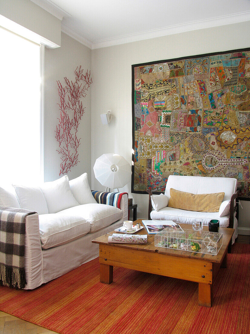 Indian wall tapestry in living room with sofa and pinewood table on striped rug
