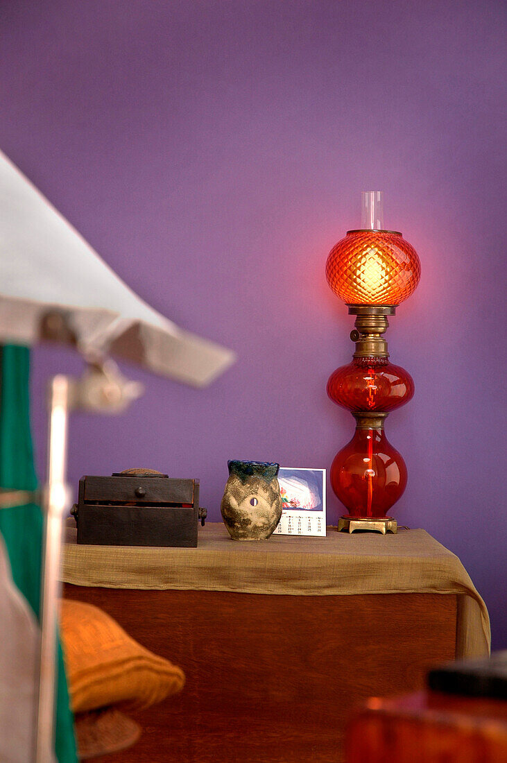 Mit Stoff bezogener Nachttisch mit roter Glaslampe vor lila Wand