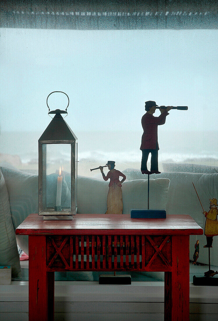 Lantern and figurines with telescopes on read painted table in beach house window