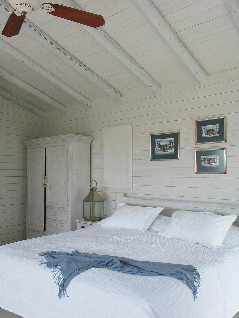 Blaue Decke auf dem Bett eines weiß gestrichenen Schlafzimmers mit Kunstwerken