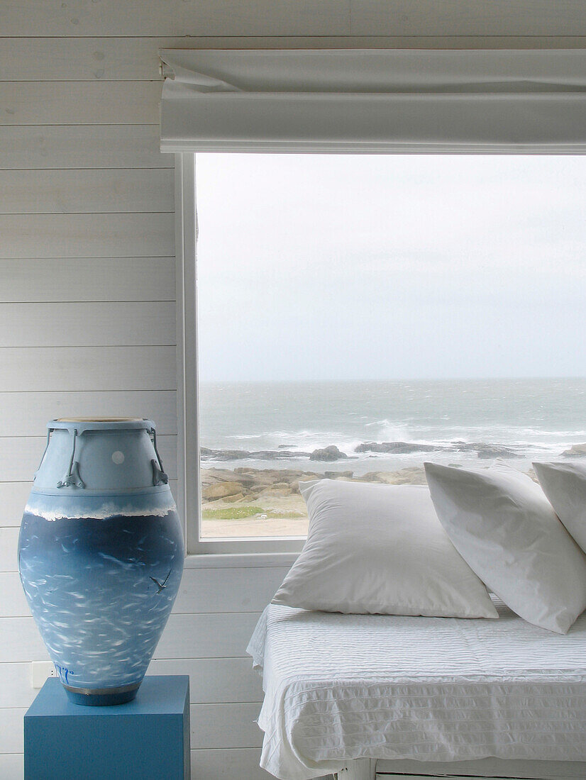 Blau gestrichene Trommel neben dem Tagesbett unter dem Fenster eines Strandhauses