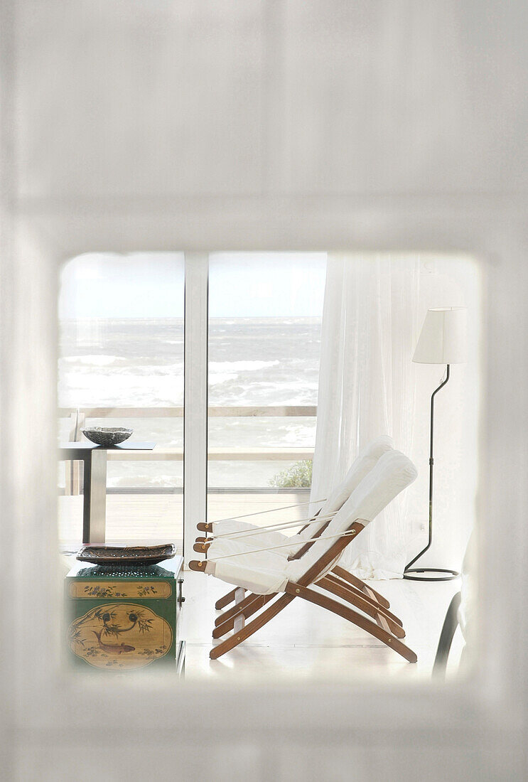 Huge windows overlooking the sea with linen curtains and a Chinese wood table lacquered in red with golden motifs sofas and deck-chairs in white canvas