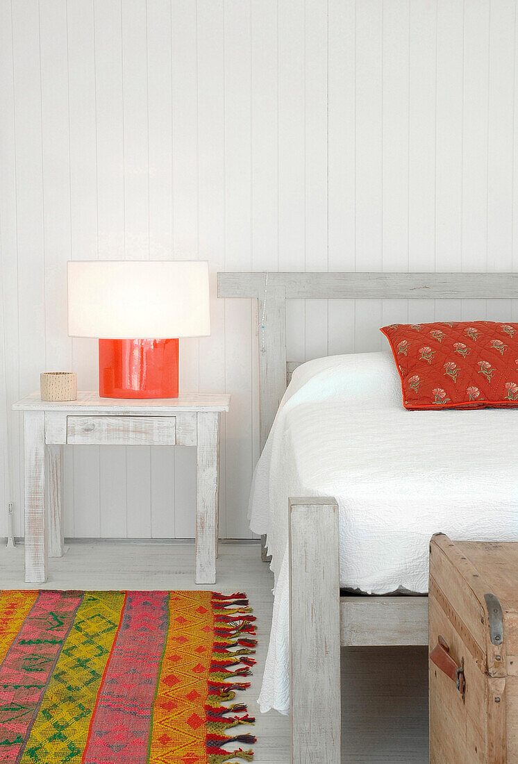 Weiße Pique-Bettdecke mit roten Kilim-Kissen, roter Keramiklampe und gemustertem Teppich
