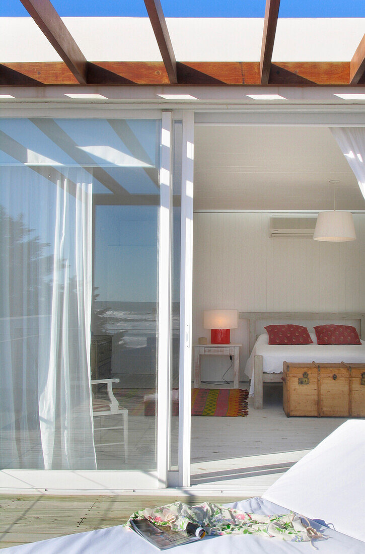 View through glass door into bedroom from veranda with sun lounger
