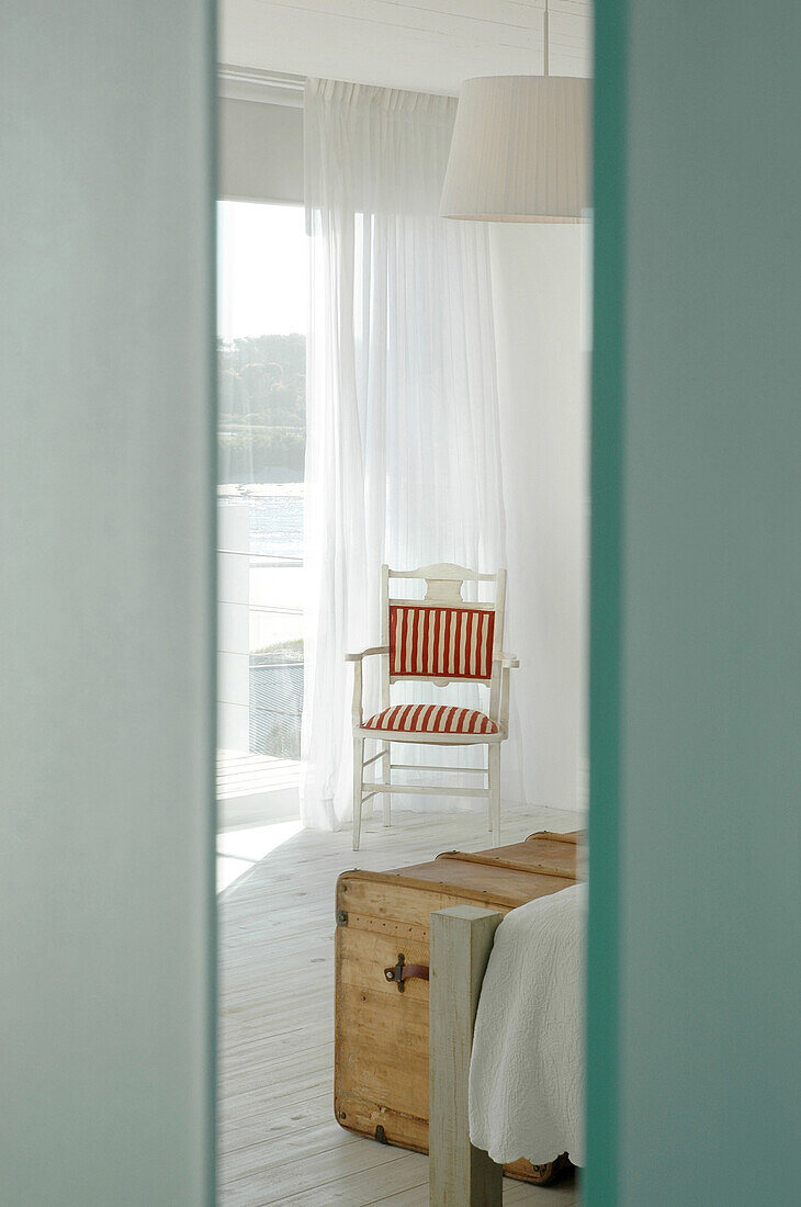 Blick in ein Schlafzimmer mit gepolstertem Reisestuhl und Hängelampe aus Ripsbändern
