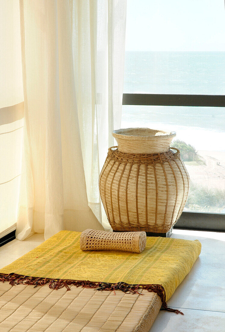 Woven basket and headrest in room corner with floor cushion and view of sea