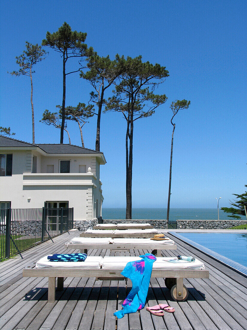 Überdachter Außenbereich am Pool eines Strandhauses mit Bäumen und Blick aufs Meer