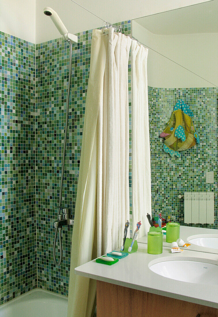 Shower fitting fixed to green mosaic tiled wall with curtain and wash basin