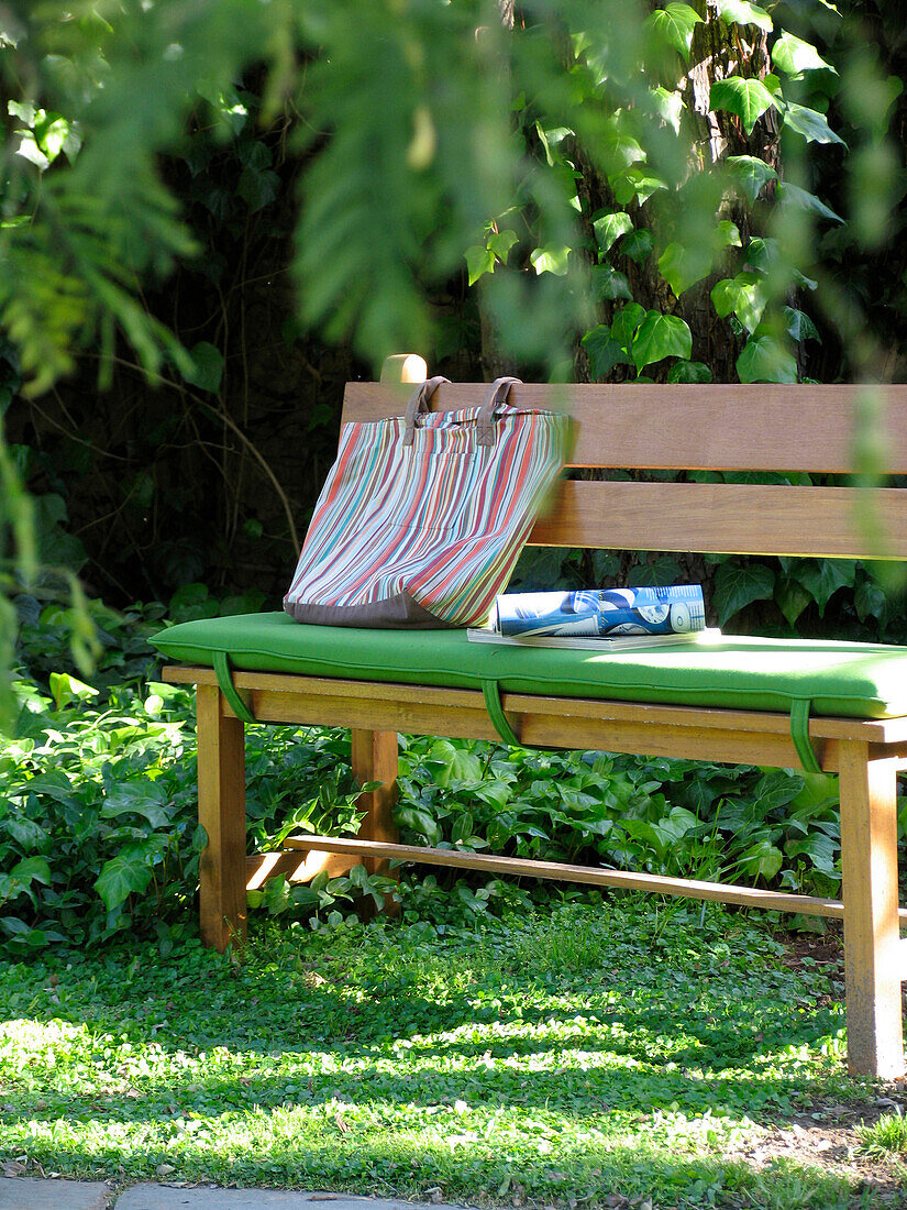 Wooden bench seat with green cushion under tree