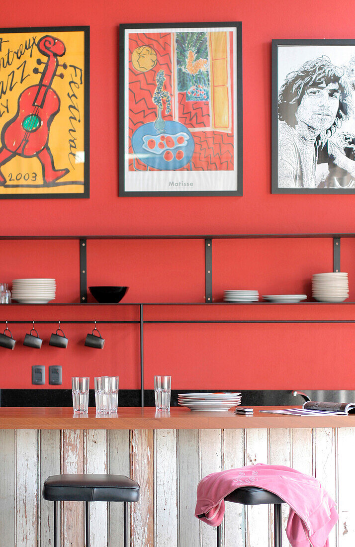 Recycelte Holztheke mit Lapacho-Platte und Eisenregalen mit Kunstwerken auf rot gestrichenen, verputzten Wänden