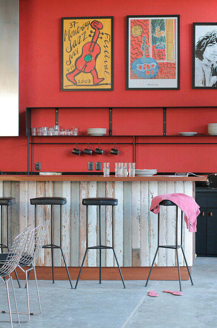 Recycelte Holztheke mit Lapacho-Platte und Eisenregalen mit Kunstwerken an rot gestrichenen, verputzten Wänden