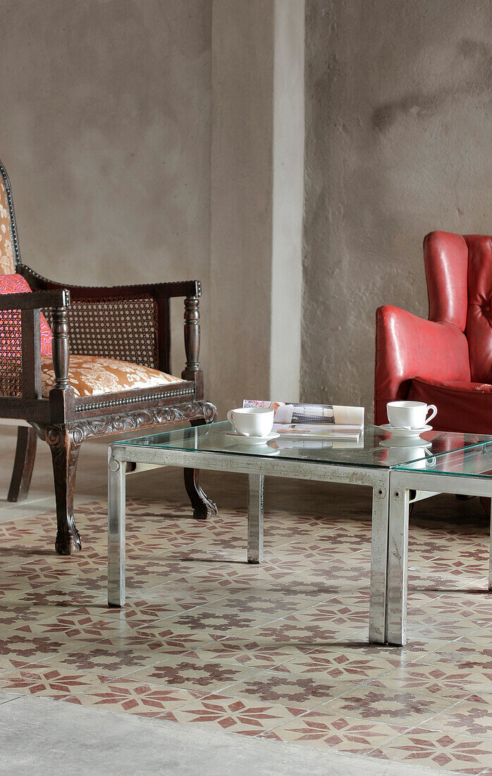 Wohnzimmer mit innovativer Matte auf Kalkfliesen, verchromtem Sessel und Tischen, die auf einer Auktion erworben wurden, und einer Wand aus unbemaltem Betonputz