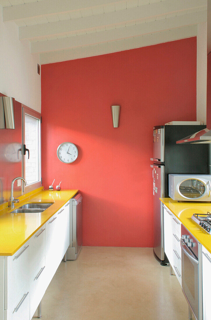 Red feature wall with clock in kitchen with yellow Formica worktops