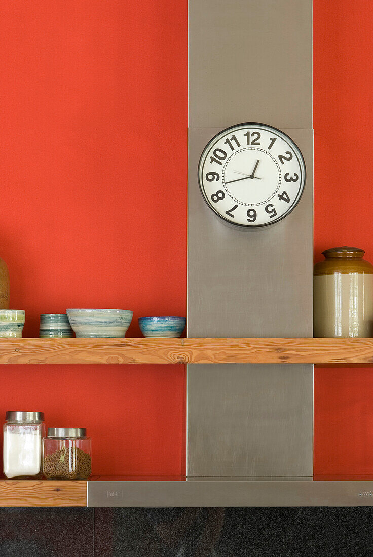Uhr auf Metallplatte mit Holzregalen in roter Küche