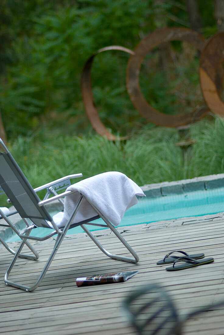 Gefaltetes Handtuch auf der Liege am Pool mit einer Zeitschrift und einem Paar Flip Flops