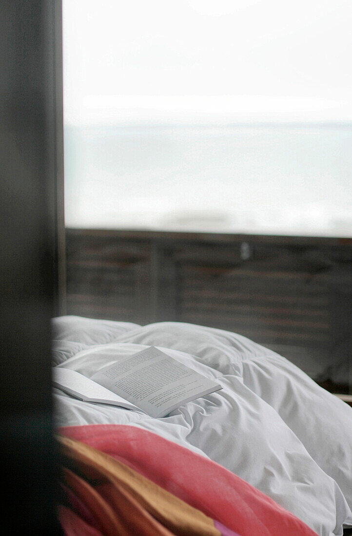 Offenes Buch auf der Bettdecke eines Strandhauses mit Blick auf das Meer