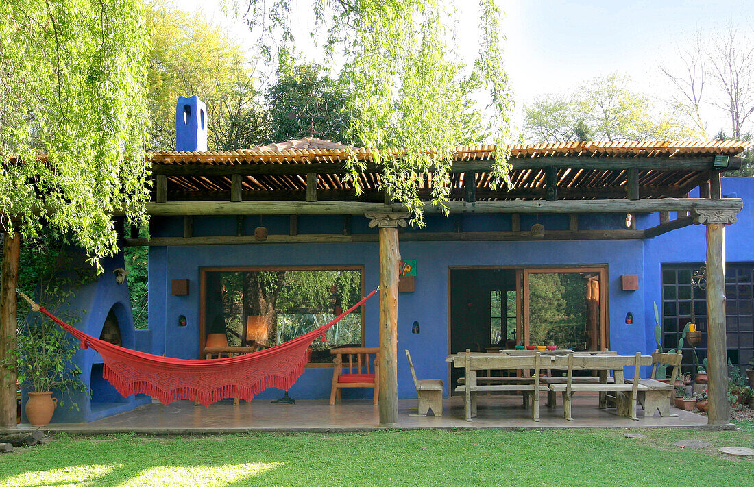 Blau gestrichene Veranda mit Markise aus Naturholz und kontrastierender roter Hängematte