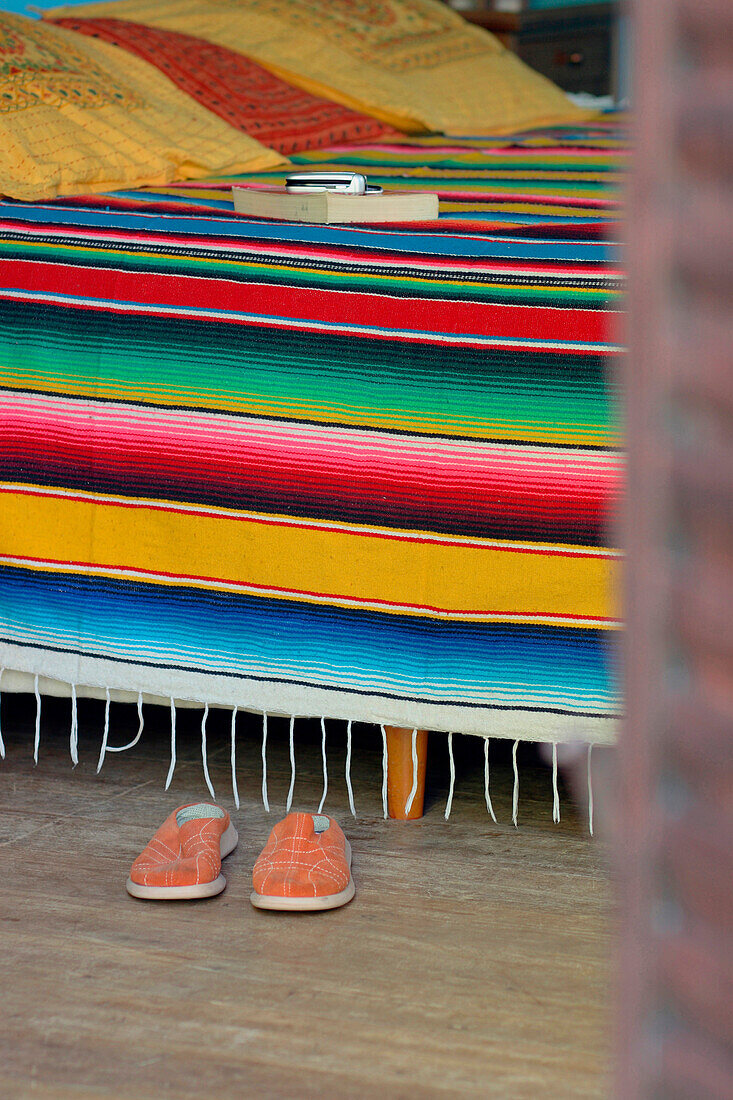 Mehrfarbige mexikanische Decke auf dem Bett mit Schuhen und einem Buch