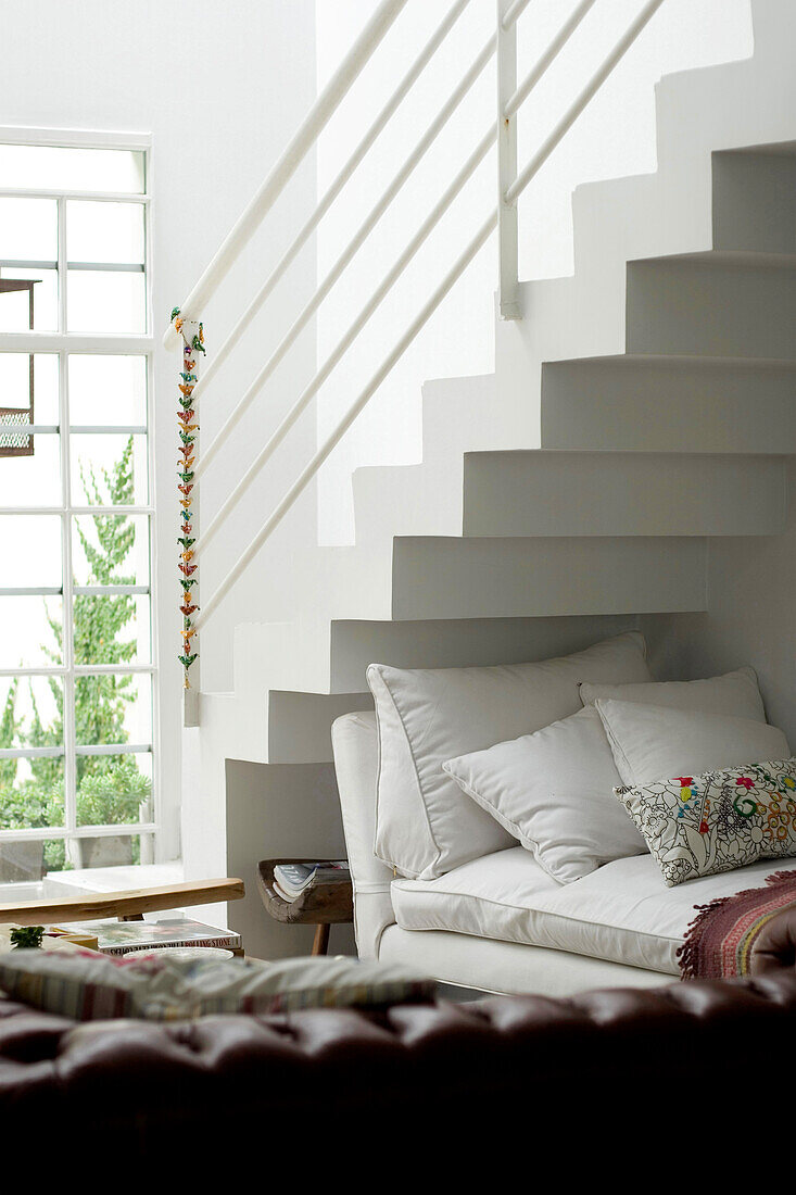 Tagesbett unter der Treppe in einer weißen Maisonettewohnung mit hängendem Ornament am Geländer